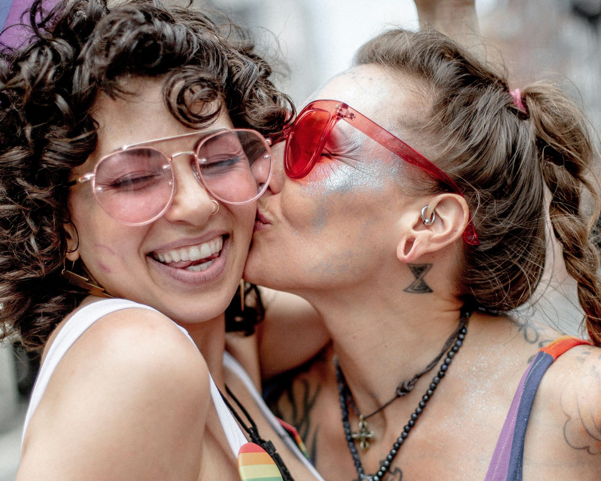 Woman kissing woman on a cheek, both wearing Pride colours